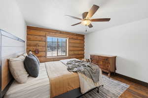 Bedroom with log walls, wood finished floors, a ceiling fan, and a textured ceiling
