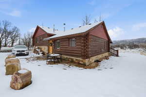 Snow covered property featuring outdoor dining area, log exterior, and stone siding