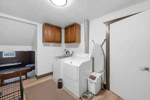 Laundry room featuring cabinet space, a textured ceiling, light wood-style flooring, and separate washer and dryer