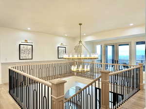 Hallway with light wood-type flooring, suspended lighting, and an upstairs landing