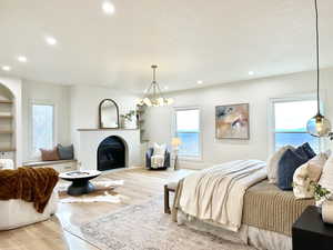 Master bedroom with wood finished floors, hanging lights, a fireplace, and a textured ceiling