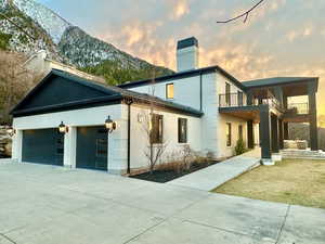 Back of house at dusk featuring a chimney, a garage, driveway, and brick siding