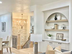 Corridor with an upstairs landing, suspended lighting, light wood-type flooring, a textured ceiling, and built in features