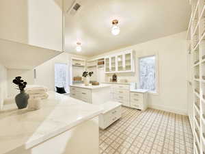 Master closet featuring white cabinetry, a center island, a textured ceiling, and glass fronted cabinets