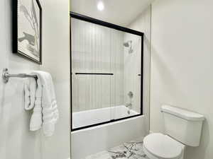 Full bathroom featuring bath / shower combo with glass door and light marble finish floors