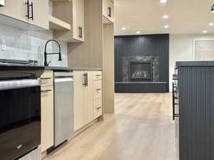 Kitchen with light wood finish cabinets, light wood-style flooring, recessed lighting, a large fireplace, and modern cabinets