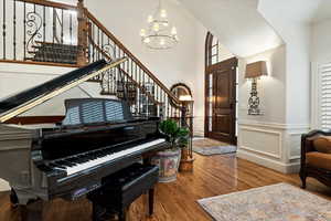 Foyer featuring dark wood-style floors, wainscoting, suspended lighting, a decorative wall, and a high ceiling