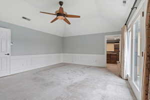 Unfurnished room with light carpet, a decorative wall, a wainscoted wall, ceiling fan, and lofted ceiling