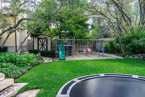 Fenced yard featuring a playground, a trampoline, a storage shed, and a patio