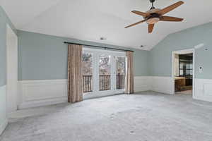 Carpeted empty room with wainscoting, a decorative wall, ceiling fan, and vaulted ceiling