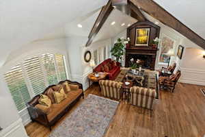 Living room with a warm lit fireplace, wood finished floors, beam ceiling, plenty of natural light, and recessed lighting