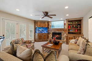 Living room featuring ceiling fan, a fireplace, recessed lighting, and light carpet