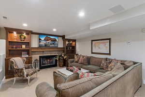 Carpeted living room featuring a fireplace with flush hearth, built in shelves, and recessed lighting