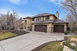 View of front of house featuring stucco siding, a chimney, concrete driveway, and stone siding