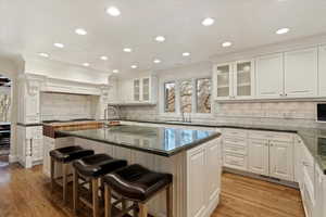 Kitchen with a breakfast bar, ornamental molding, a kitchen island with sink, dark stone countertops, and recessed lighting