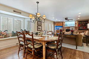 Dining space with hanging lights, a stone fireplace, light wood-style flooring, and a ceiling fan