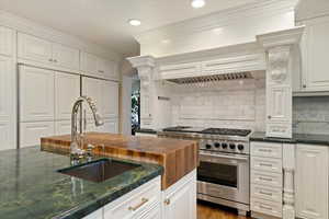Kitchen with luxury range, white cabinetry, dark stone countertops, ornamental molding, and decorative backsplash