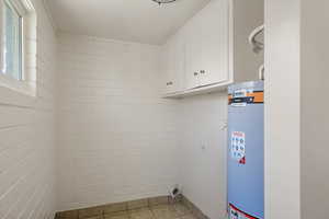 Laundry room with gas water heater, cabinet space, and light tile patterned floors