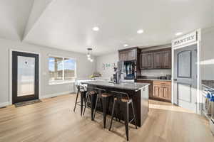 Kitchen with dark wood finish cabinetry, light stone countertops, a center island with sink, a kitchen breakfast bar, and light wood-style flooring