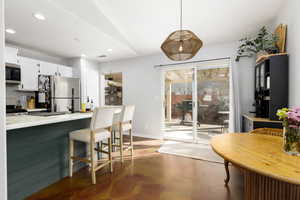Kitchen featuring white cabinets, light countertops, stainless steel appliances, a kitchen breakfast bar, and concrete floors