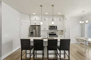 Kitchen featuring stainless steel appliances, an island with sink, white cabinets, and solid surface counters