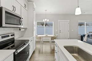 Open kitchen with stainless steel appliances, wood-style flooring, solid surface counters, and tile backsplash