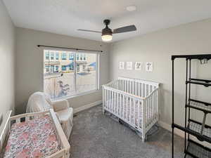 Bedroom with a crib, dark colored carpet, and ceiling fan
