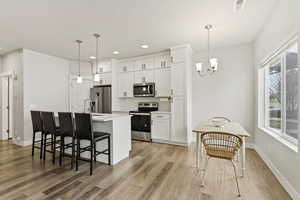 Kitchen with stainless steel appliances, a breakfast bar area, white cabinetry, light wood finished floors, and tasteful backsplash