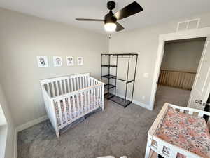 Carpeted bedroom with a crib and ceiling fan