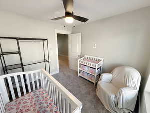 Carpeted bedroom featuring a crib and a ceiling fan