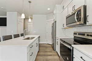 Kitchen featuring stainless steel appliances, an island with sink, white cabinets, and light solid surface counters