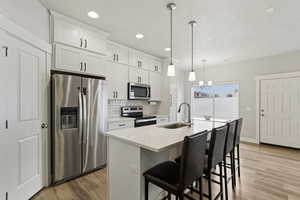 Kitchen featuring stainless steel appliances, white cabinetry, light wood-style flooring, and a textured ceiling