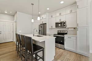 Kitchen featuring white cabinetry, a kitchen bar, stainless steel appliances, LVP floors, and a center island with sink