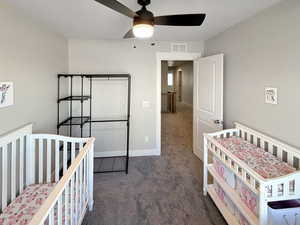 Bedroom with a nursery area, dark colored carpet, and ceiling fan