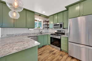 Kitchen featuring green cabinetry, stainless steel appliances, granite countertops, light wood-type flooring, and open shelves