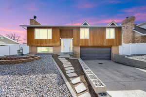 Raised ranch featuring concrete driveway, a garage, a chimney, and a gate