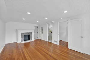 Unfurnished living room with built in shelves, light wood-type flooring, a textured ceiling, and a fireplace with raised hearth