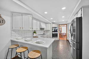 Kitchen featuring a breakfast bar, white cabinetry, stainless steel appliances, a peninsula, and recessed lighting