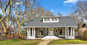 View of front of home with brick siding, a front yard, roof with shingles, and covered porch