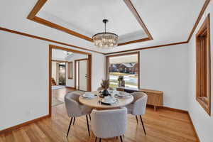 Dining area featuring suspended lighting, crown molding, light wood-type flooring, and a tray ceiling