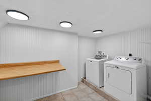 Laundry area with a textured ceiling, washing machine and dryer, and light tile patterned floors