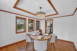 Dining room with a tray ceiling, suspended lighting, light wood finished floors, and ornamental molding