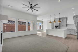 Kitchen featuring gray cabinets, ceiling fan, an island with sink, light stone countertops, and tasteful backsplash