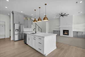 Kitchen with stainless steel appliances, open floor plan, a large fireplace, an island with sink, and glass insert cabinets