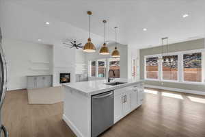 Kitchen featuring a large fireplace, open floor plan, stainless steel appliances, light wood-type flooring, and a center island with sink