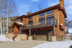 View of front of property featuring a garage, stone siding, a deck, and a chimney