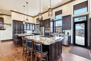 Kitchen with a high ceiling, a breakfast bar, dark wood finish cabinetry, light wood-style flooring, and stainless steel appliances