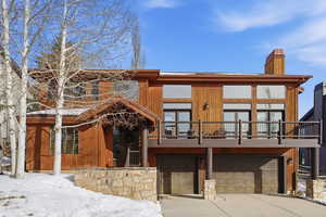 View of front of home featuring an attached garage, a chimney, a balcony, concrete driveway, and stone siding