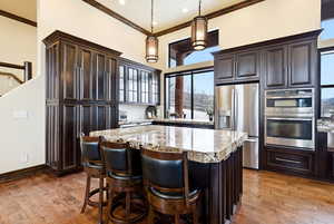 Kitchen with stainless steel appliances, dark wood finish cabinets, a center island, a kitchen breakfast bar, and ornamental molding