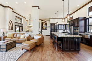 Kitchen featuring a high ceiling, light stone countertops, light wood-type flooring, a breakfast bar area, and stainless steel appliances